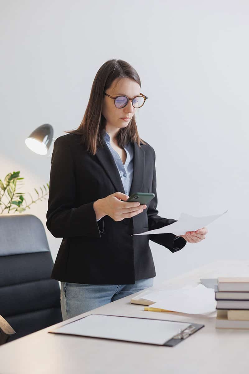 Lawyer in a black blazer reviewing documents and checking her phone, symbolizing responsiveness.