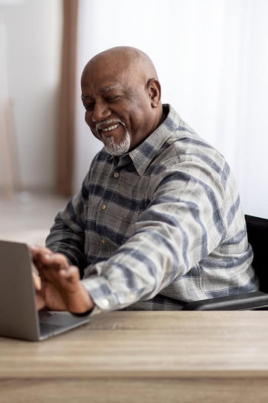 Elderly man smiling while working on a laptop as part of proactive Medicaid planning.