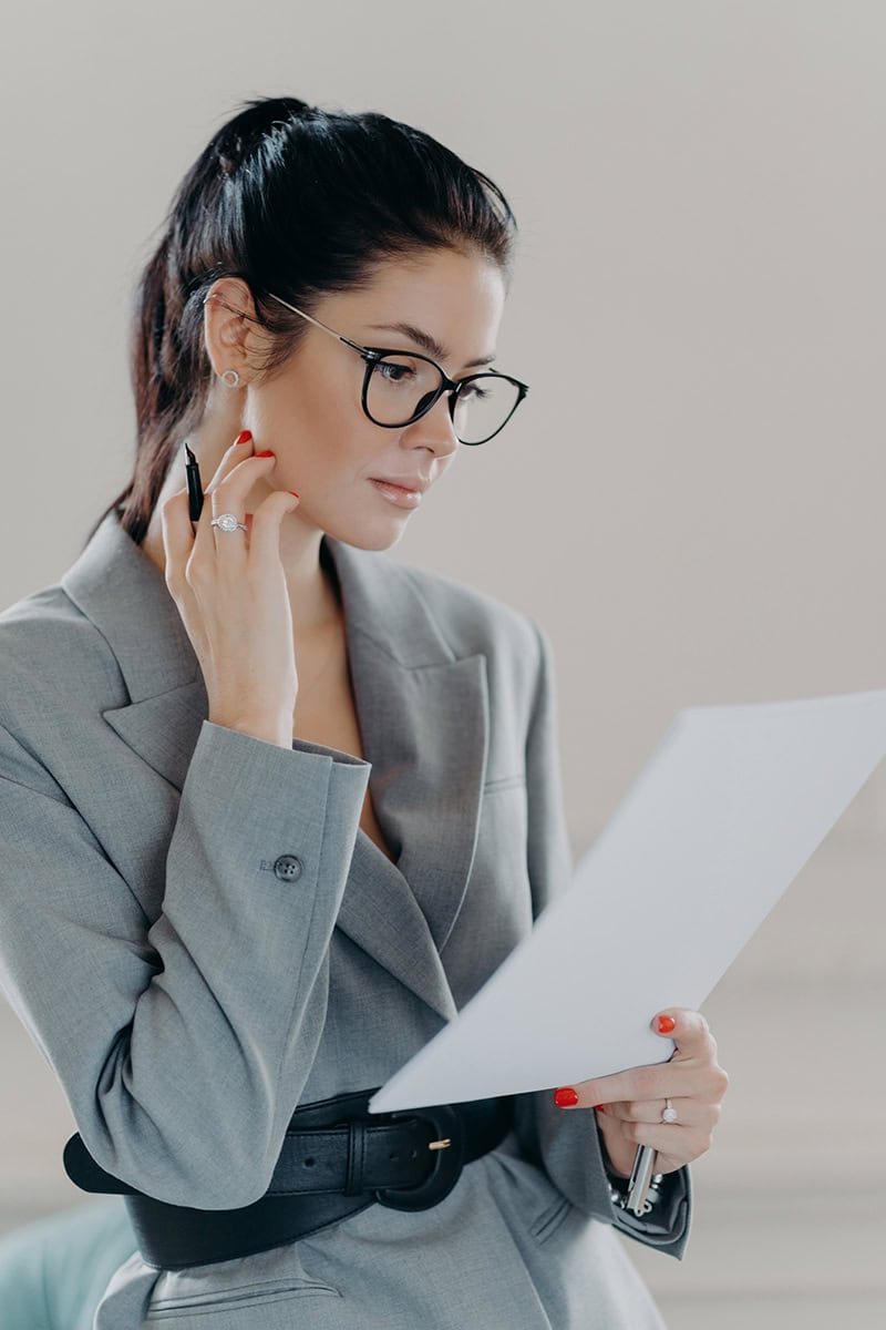 Female lawyer in glasses carefully reviewing legal documents with attention to detail.