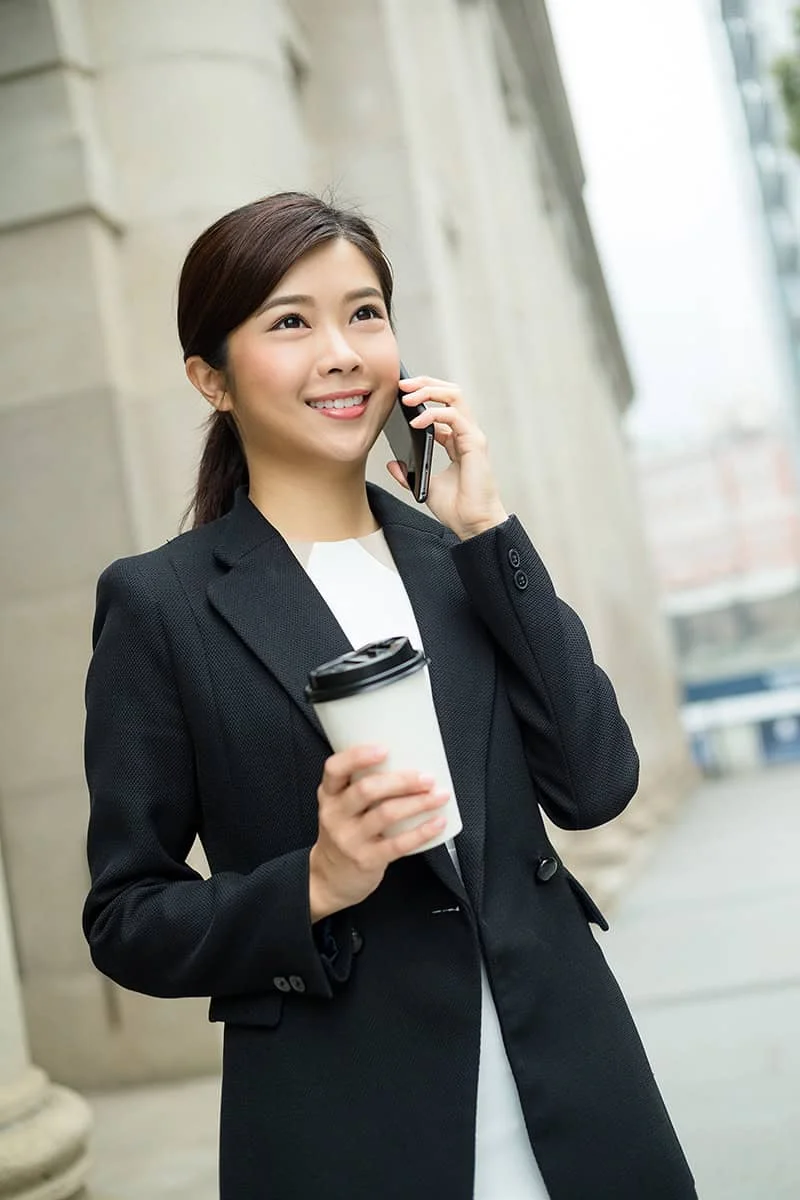 Smiling lawyer in a black suit holding a coffee cup and speaking on the phone.