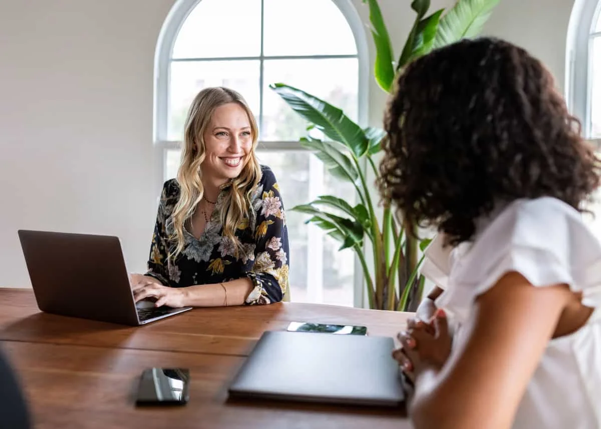 Smiling woman meeting with another woman in a bright office to discuss estate planning for single people and using their laptop